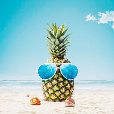 Funny pineapple with sunglasses sunbathing at the beach, summer vacations concept, copy space