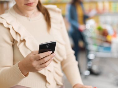 Müşteri süpermarkette alışveriş yapıyor ve akıllı telefonunu kullanıyor.