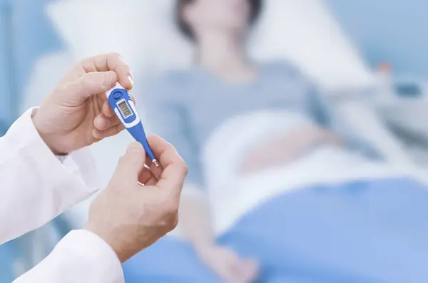 Doctor taking a patient\'s temperature using a digital thermometer, the patient is lying on the bed