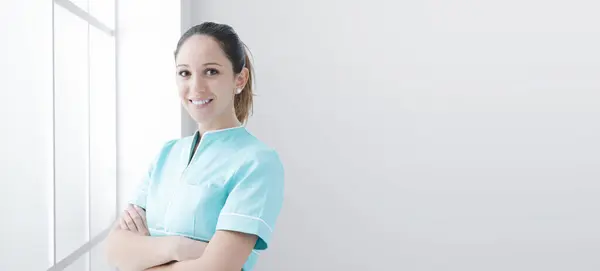 在医院工作的年轻而自信的女护士 双手交叉 面带微笑地摆姿势 — 图库照片