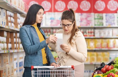 Süpermarkette hayal kırıklığına uğramış kadınlar, birlikte pahalı bir market fişini, bütçe ve market alışverişini kontrol ediyorlar.
