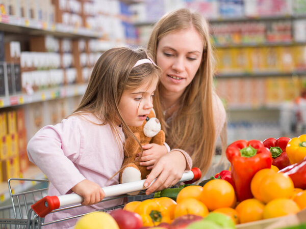 Mother and daughter doing grocery shopping together, they are choosing fruits and vegetables in the produce section