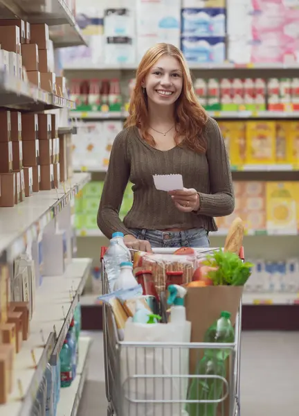 Молодая Улыбающаяся Женщина Делающая Покупки Супермаркете Толкает Полный Тележку Держит — стоковое фото