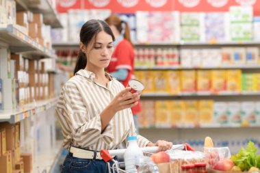 Kadın elinde kutu tutuyor ve markette beslenme bilgileri okuyor. Market alışverişi ve beslenme konsepti.