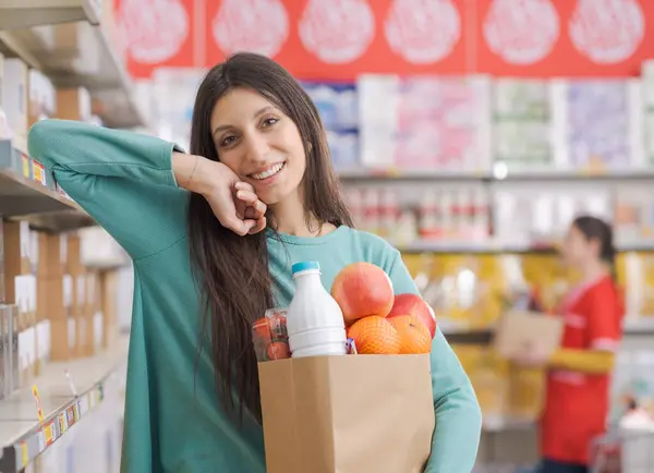 スーパーマーケットの食料品でいっぱいの袋を持っている幸せな若い女性の肖像画 彼女はカメラで微笑んでいる — ストック写真