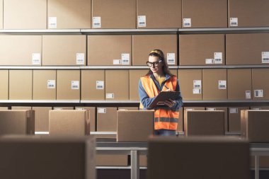 Depoda paket ve siparişleri kontrol eden genç bir bayan işçi.