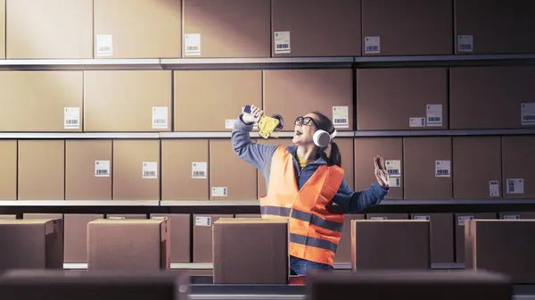 stock image Cheerful distracted warehouse employee singing and dancing instead of working, she is dreaming of a new life and she wants to change her career