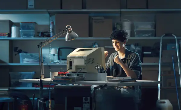 stock image Cheerful happy teenager in his garage, he is playing with an old computer and celebrating with raised fists