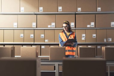 Depoda paket ve siparişleri kontrol eden genç bir bayan işçi.