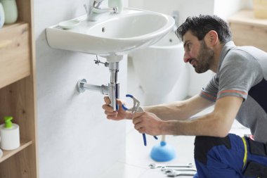 Tesisatçı banyo lavabosunu kontrol ediyor ve su pompası kullanıyor.