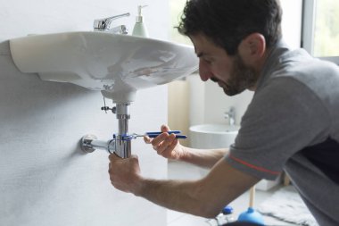 Profesyonel tesisatçı banyo lavabosunu tamir ediyor, kerpeten kullanıyor.