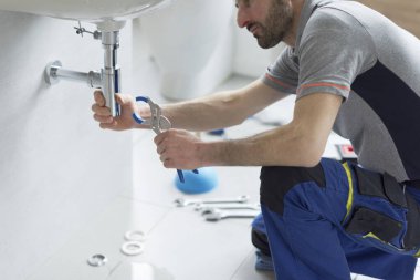 Tesisatçı banyo lavabosunu kontrol ediyor ve su pompası kullanıyor.