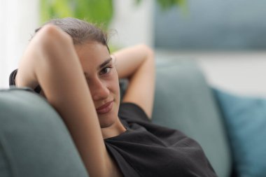 Evdeki kanepede dinlenen sevimli genç bayan kameraya gülümsüyor.