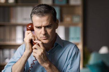 Endişeli iş adamı ofisinde telefonla konuşuyor.