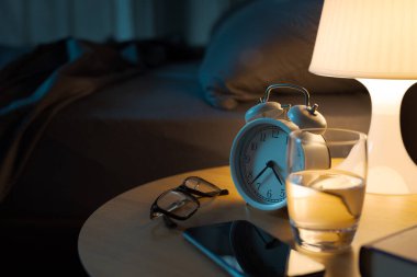 Kişisel eşyalar ve lamba yatak odasındaki komodinin üzerinde, yatak da arka planda.