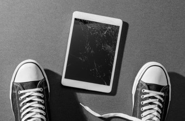 Kırık dijital tablet ve genç adam ayağı. Cihazı düşürdü. Onarıma ihtiyacı var.