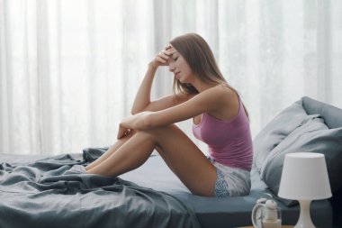 Sabahları yatakta oturan üzgün genç bir kadın endişeli ve hayal kırıklığına uğramış olduğunu düşünüyor.