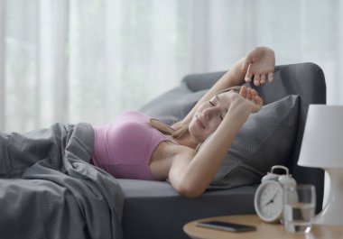 Genç ve güzel bir kadın sabah yatağında uzanıyor ve uyanıyor, gülümsüyor ve kollarını açıyor.