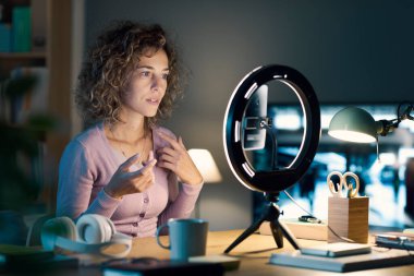 Profesyonel nüfuzlu kişi masasında oturuyor ve sosyal medya profilleri için bir video içeriği kaydediyor, bir akıllı telefon ve halka ışığı kullanıyor: sosyal medya ve iletişim konsepti