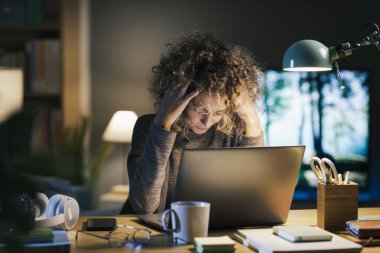 Geç saatlere kadar bilgisayarında çalışan genç bir kadın, yorgun ve baş ağrısı, teslim tarihleri ve tükenme konsepti yaşıyor.
