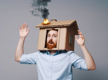 Kafası yanan bir karton evin içinde haykırırken şok olmuş ev sahibi: emlak sigortası, yangınlar, kazalar ve felaketler konsepti