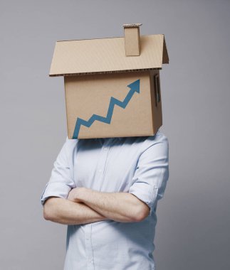 Kafasında karton ev olan ve büyüyen finansal tablosu yukarı bakan bir adam, konut piyasası eğilimi konsepti
