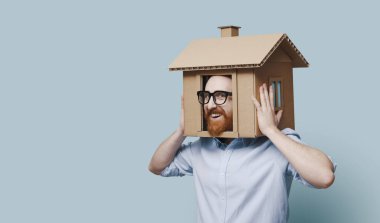 Kartondan minyatür bir evde kafası olan güler yüzlü bir adam: gayrimenkul, konut ve sigorta çözümleri kavramı