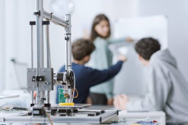 Laboratuvarda birlikte çalışan zeki mühendislik öğrencileri, beyaz tahtadaki bir projeyi kontrol ediyorlar ve konuşuyorlar, ön planda 3D yazıcı ve araçlar var.