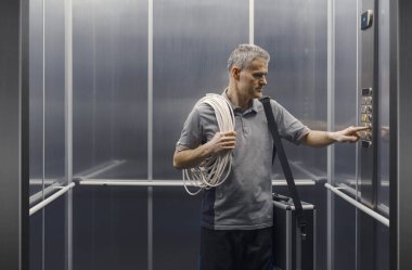 Profesyonel elektrikçi asansörde duruyor ve kontrol panelinin düğmesine basıyor.