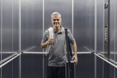 Asansörde duran ve kameraya gülümseyen profesyonel elektrikçi.