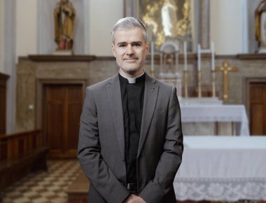 Papaz kıyafeti giymiş orta yaşlı kendinden emin bir rahibin portresi bir kilisenin içinde duruyor.