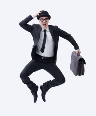 Elinde evrak çantası olan koyu renk takım elbiseli bir işadamı başarısını kutlarken sevinçle atlıyor..