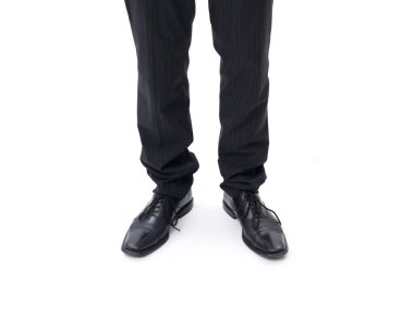 Koyu takım elbiseli adam ayakta, ayakkabılarına yakın, beyaz arka planda izole edilmiş.