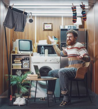 Mikro bir dairede yaşayan mutlu bekar bir adamın portresi: Kahve içiyor ve kameraya gülümsüyor