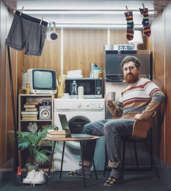 Mikro bir dairede yaşayan mutlu bekar bir adamın portresi: Kahve içiyor ve kameraya gülümsüyor