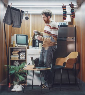 Genç adam mikro bir dairede tek başına yaşıyor, bir fincana kahve dolduruyor ve kahvaltı yapıyor.