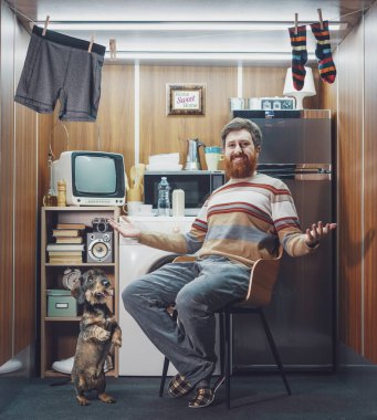 Çok küçük bir stüdyo dairede köpeğiyle yalnız yaşayan mutlu bir adamın portresi, kameraya gülümsüyor ve evini gösteriyor.
