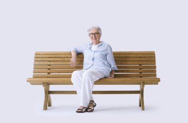 Gülümseyen ve mutlu yaşlı kadın bankta oturmuş kameraya bakıyor..