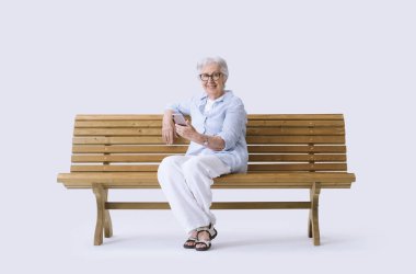 Gülümseyen ve mutlu yaşlı bir kadın cep telefonuyla kameraya bakıyor..