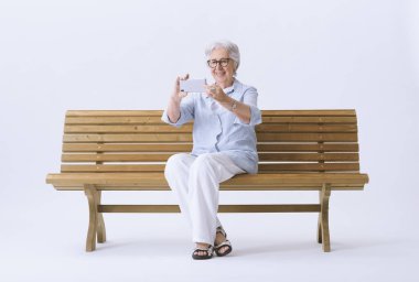 Gülümseyen ve mutlu yaşlı bir kadın telefonuyla fotoğraf çekiyor..