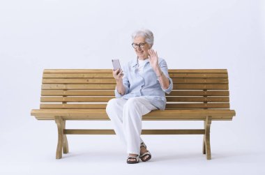 Gülümseyen ve mutlu yaşlı bir kadın telefonundaki video görüşmesi sırasında el sallıyor..