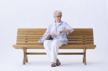 Bankta oturan yaşlı bir kadın saatine bakıyor..