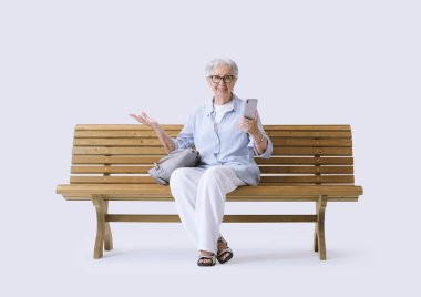 Gülümseyen ve mutlu yaşlı bir kadın cep telefonuyla kameraya bakıyor..