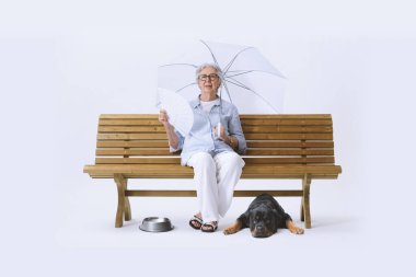 Beyaz şemsiyeli yaşlı bir kadın, bankta oturuyor, kendini serinletirken sıcaktan muzdarip. Küresel ısınma kavramı.