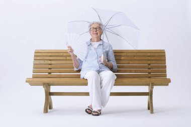 Beyaz şemsiyeli yaşlı bir kadın, bankta oturuyor, kendini serinletirken sıcaktan muzdarip. Küresel ısınma kavramı.
