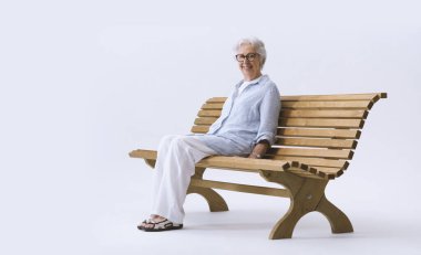 Gülümseyen ve mutlu yaşlı kadın bankta oturmuş kameraya bakıyor..