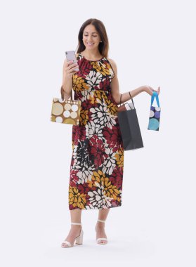 Güzel, gülümseyen genç bir kadın elinde telefonuyla ve birkaç alışveriş çantasıyla beyaz arka planda poz veriyor..