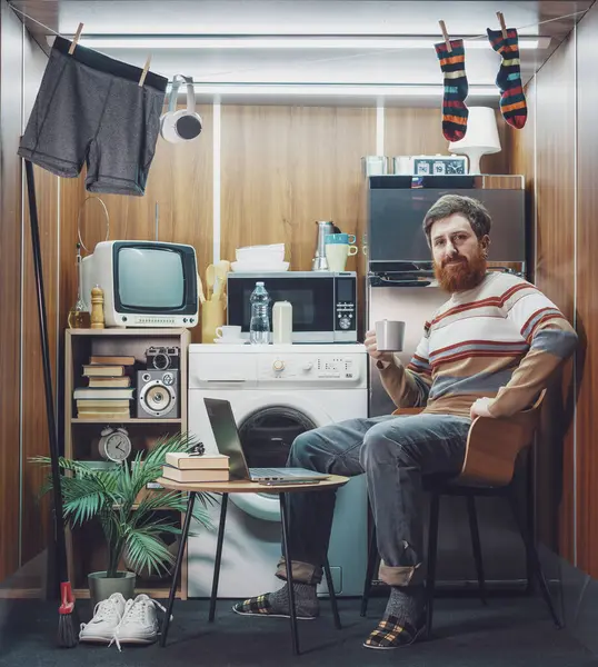 Mikro bir dairede yaşayan mutlu bekar bir adamın portresi: Kahve içiyor ve kameraya gülümsüyor