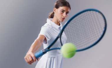 Atletik genç tenisçi güçlü bir ters vuruş yapıyor, odaklanmayı, hareketi ve enerjiyi vurgulamak için tarafsız bir arkaplanda izole edilmiş..