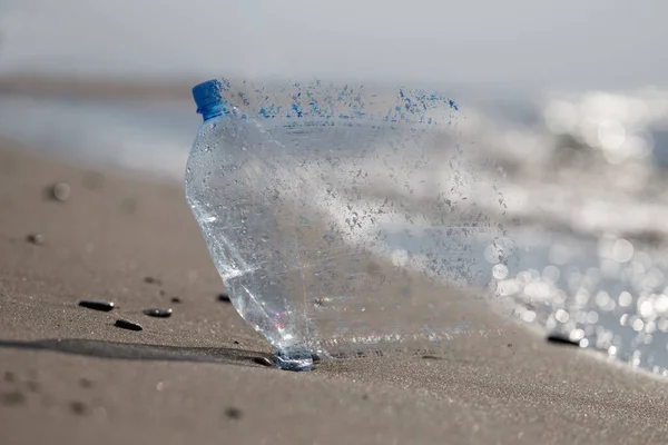 The problem of micro plastic pollution, conceptual image. Plastic bottle on the beach absorbed by the ocean.